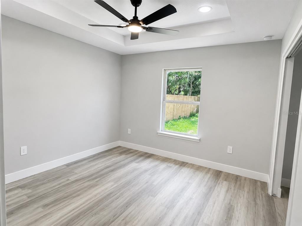 A bedroom with light gray walls, wood-look flooring, a tray ceiling, and built-in shelving — 12744 SE 102ND TERRACE, BELLEVIEW, FL