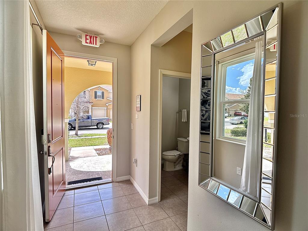 An entryway features a tiled floor, an open front door, a bathroom, and a decorative mirror — 5117 KILLARNEY WAY, KISSIMMEE, FL