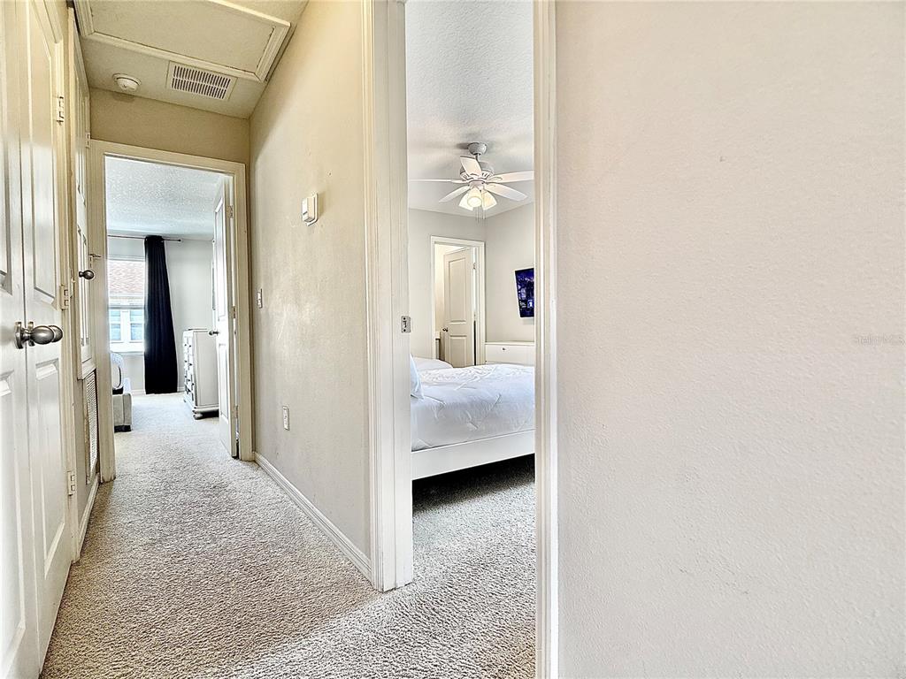 A hallway with carpeted floors leads to two bedrooms with white doors and ceiling fans — 5117 KILLARNEY WAY, KISSIMMEE, FL
