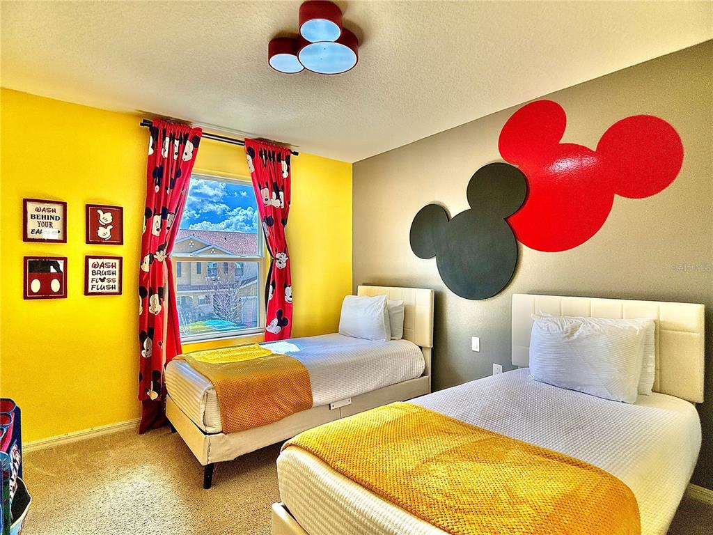 A bedroom features two twin beds, yellow walls, and Mickey Mouse-themed decor and light fixtures — 5117 KILLARNEY WAY, KISSIMMEE, FL