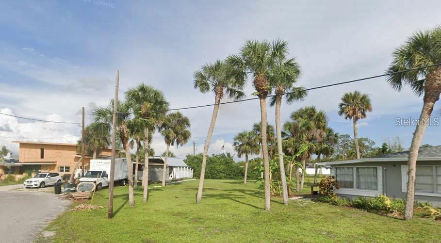 A grassy lot with several palm trees sits between a house and a construction site — ROSE STREET, VENICE, FL