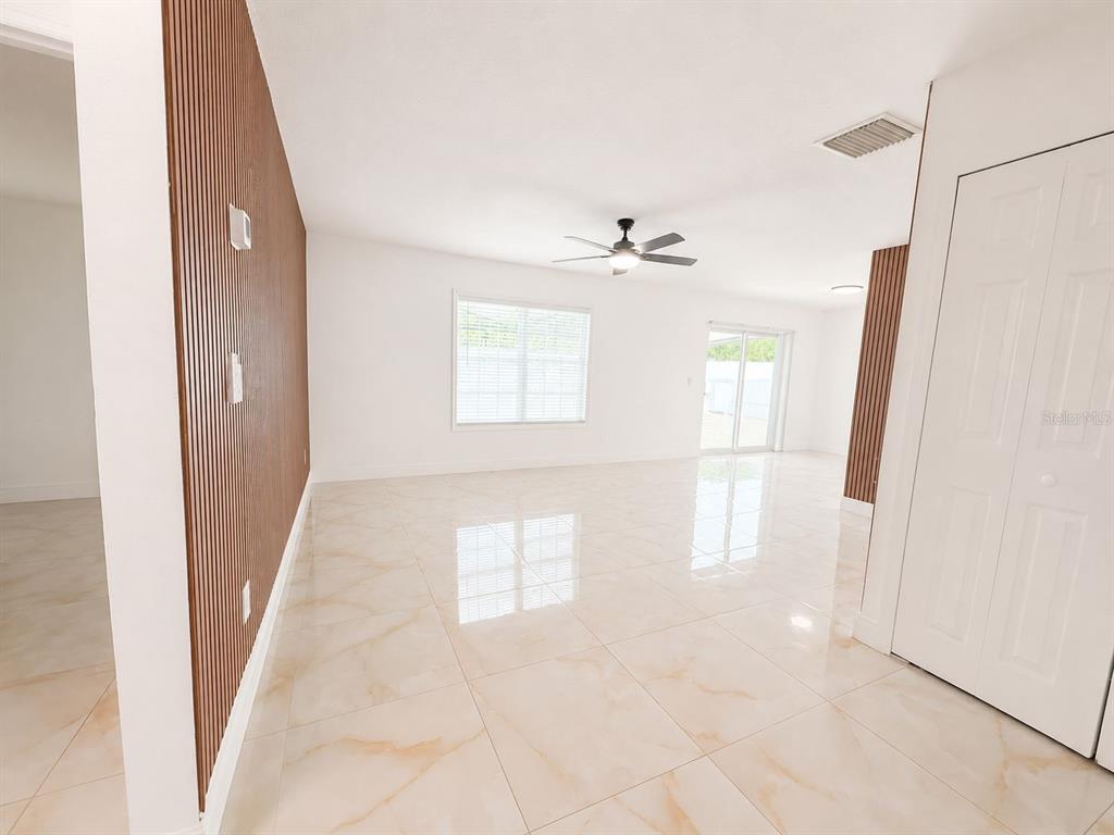 A bright living room features large light-colored floor tiles and a wood-slat accent wall — 9203 CAMINO VILLA BOULEVARD, TAMPA, FL