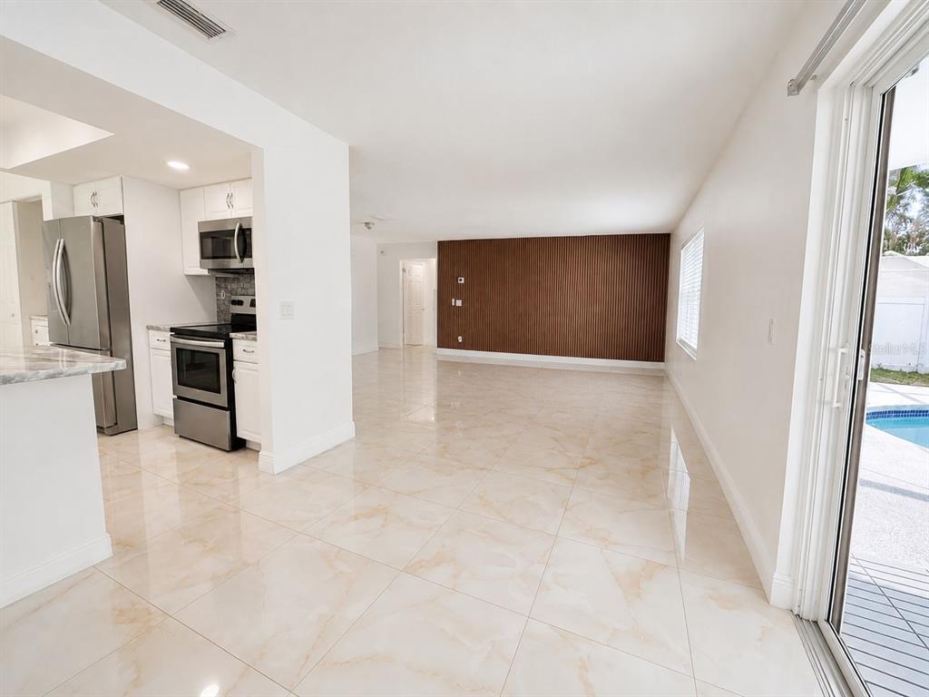 A kitchen with stainless steel appliances opens to a living area with a wood-slatted wall — 9203 CAMINO VILLA BOULEVARD, TAMPA, FL