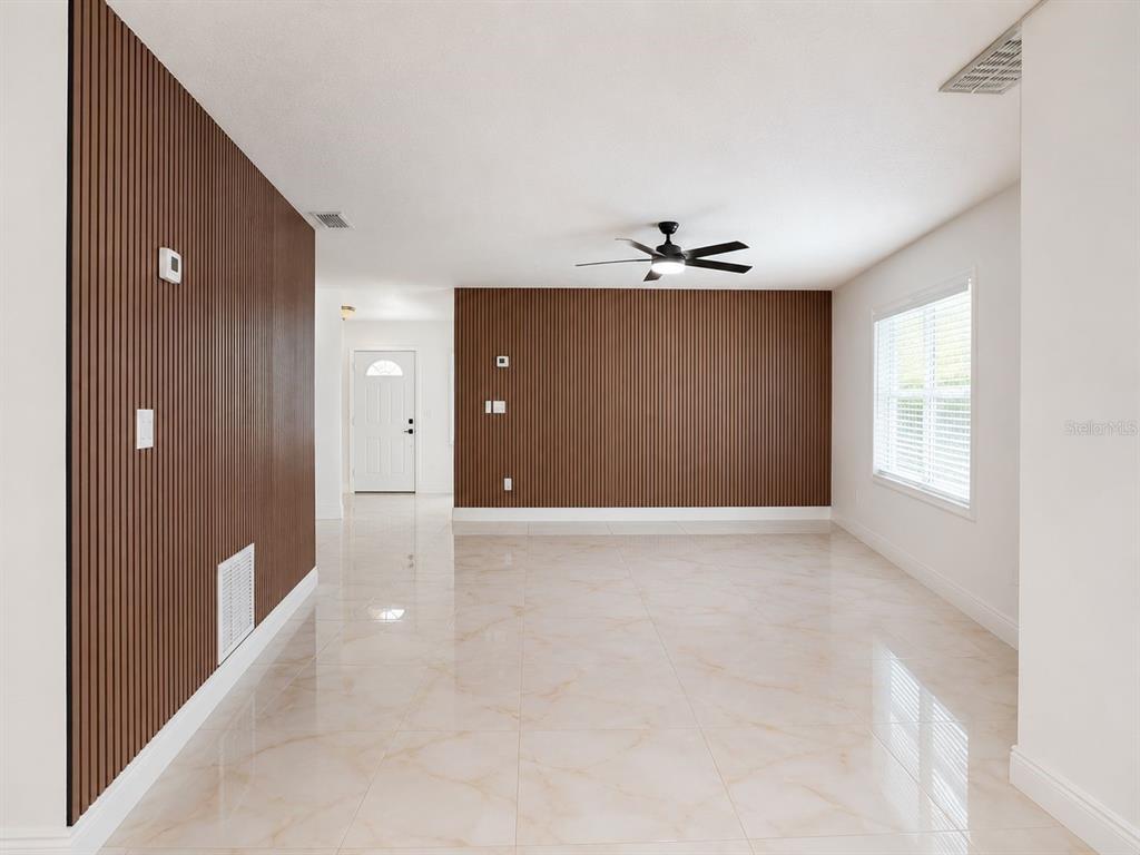 A room with light-colored tile floors and dark wood-slat accent walls under a ceiling fan — 9203 CAMINO VILLA BOULEVARD, TAMPA, FL