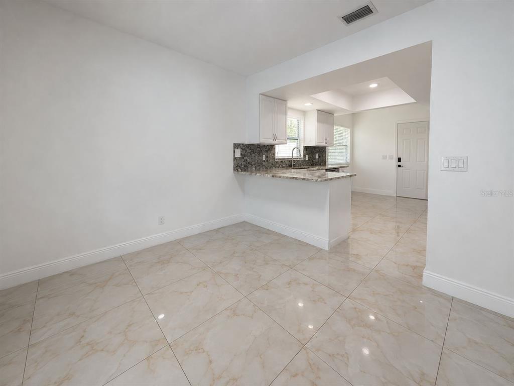 A kitchen with white cabinets and a granite breakfast bar overlooks a tiled dining area — 9203 CAMINO VILLA BOULEVARD, TAMPA, FL