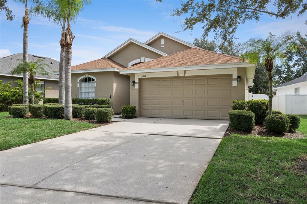 A single-story house with a tan stucco exterior, a two-car garage, and manicured landscaping — 9957 CYPRESS VINE DRIVE, ORLANDO, FL