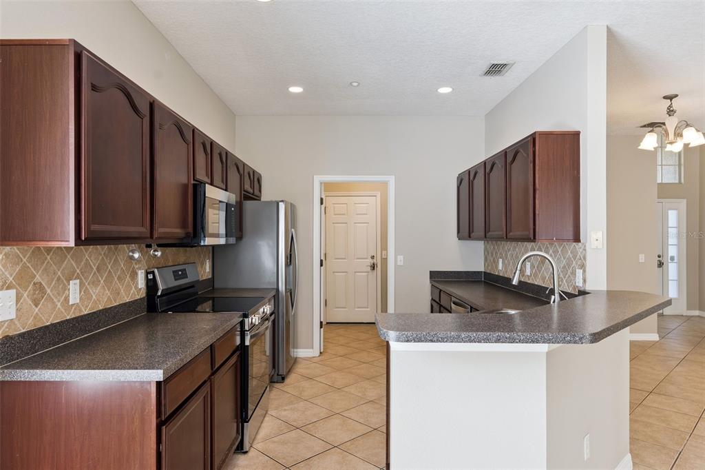 A kitchen with dark wood cabinets, granite countertops, stainless steel appliances, and tile flooring — 9957 CYPRESS VINE DRIVE, ORLANDO, FL