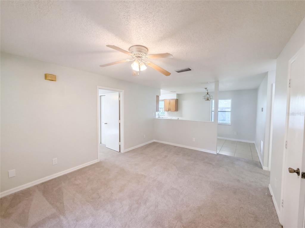 A living room with beige carpet, a ceiling fan, and an open view into a kitchen — 32444 OKALOOSA TRAIL, SORRENTO, FL
