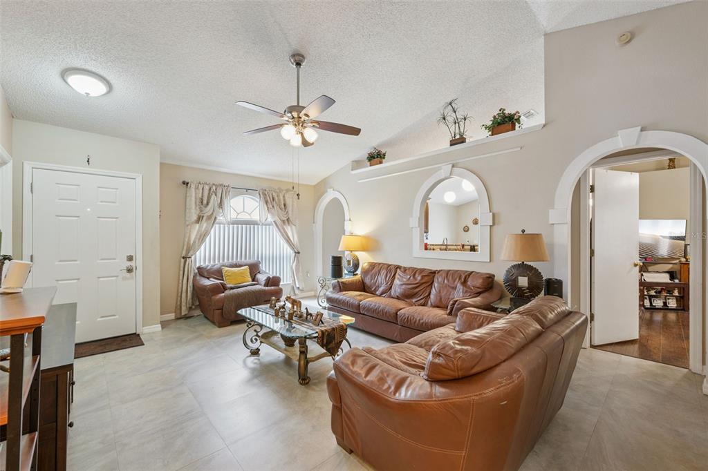 A living room features tile flooring, brown leather furniture, a ceiling fan, and arched wall accents — 10044 RICHARDSON COURT, ORLANDO, FL