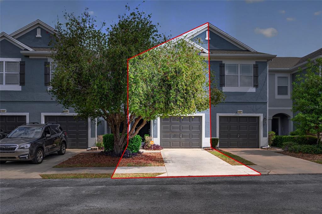 A two-story townhouse exterior with a gray garage, a concrete driveway, and a large tree — 4954 SW 45TH CIRCLE, OCALA, FL