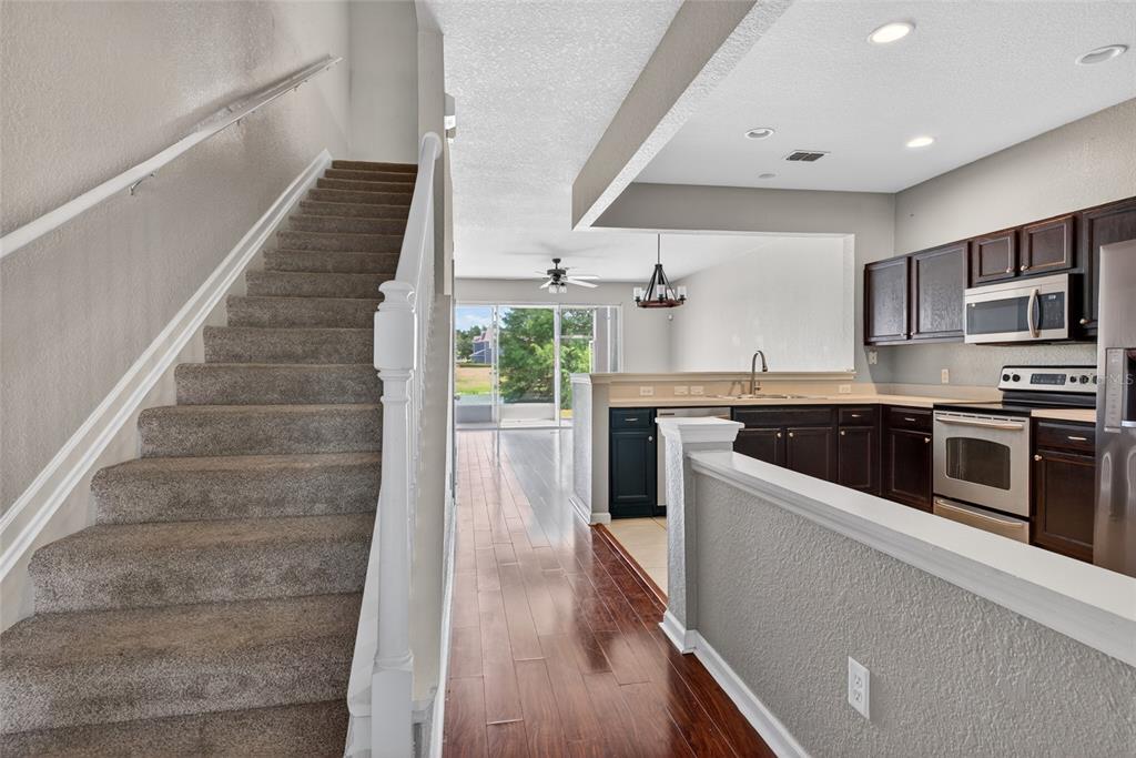 A carpeted staircase sits beside a kitchen with dark cabinets and wood flooring — 4954 SW 45TH CIRCLE, OCALA, FL