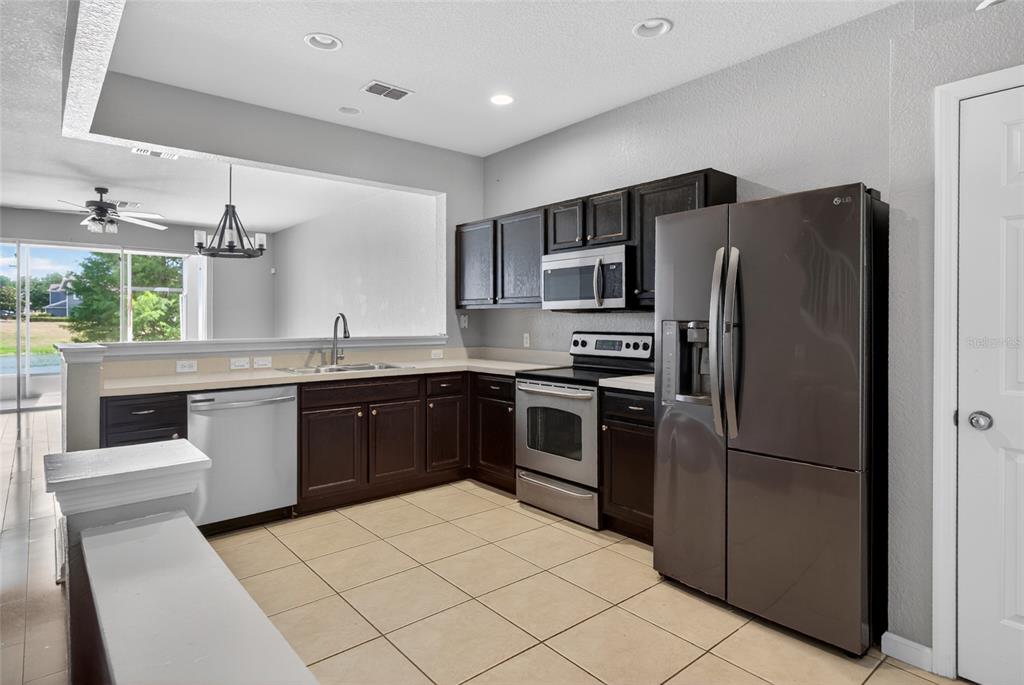 A kitchen features dark wood cabinets, stainless steel appliances, and tile flooring — 4954 SW 45TH CIRCLE, OCALA, FL
