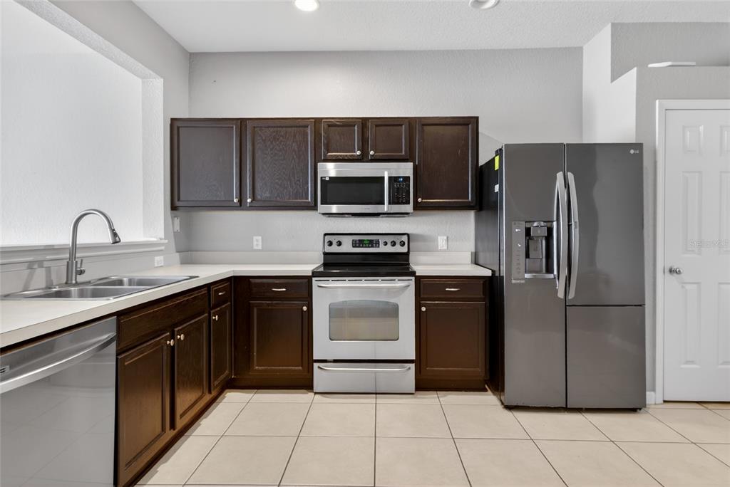 A kitchen features dark wood cabinets, stainless steel appliances, white countertops, and light tile flooring — 4954 SW 45TH CIRCLE, OCALA, FL