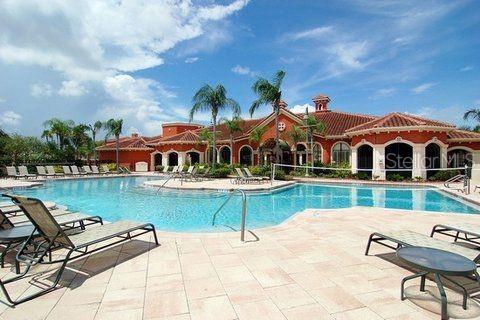 A swimming pool with lounge chairs sits in front of a large, Mediterranean-style clubhouse — 2739 VIA CAPRI UNIT 1014, CLEARWATER, FL