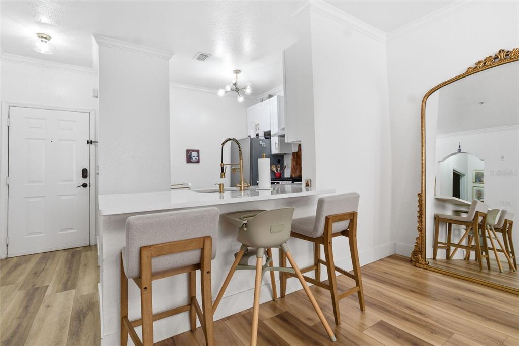 A kitchen with white cabinets and a breakfast bar featuring three stools and a mirror — 2739 VIA CAPRI UNIT 1014, CLEARWATER, FL