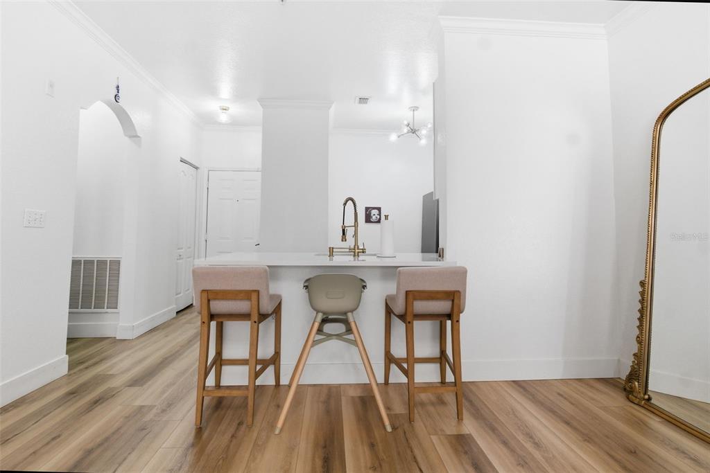 A kitchen island with three stools sits in a room with white walls and flooring — 2739 VIA CAPRI UNIT 1014, CLEARWATER, FL