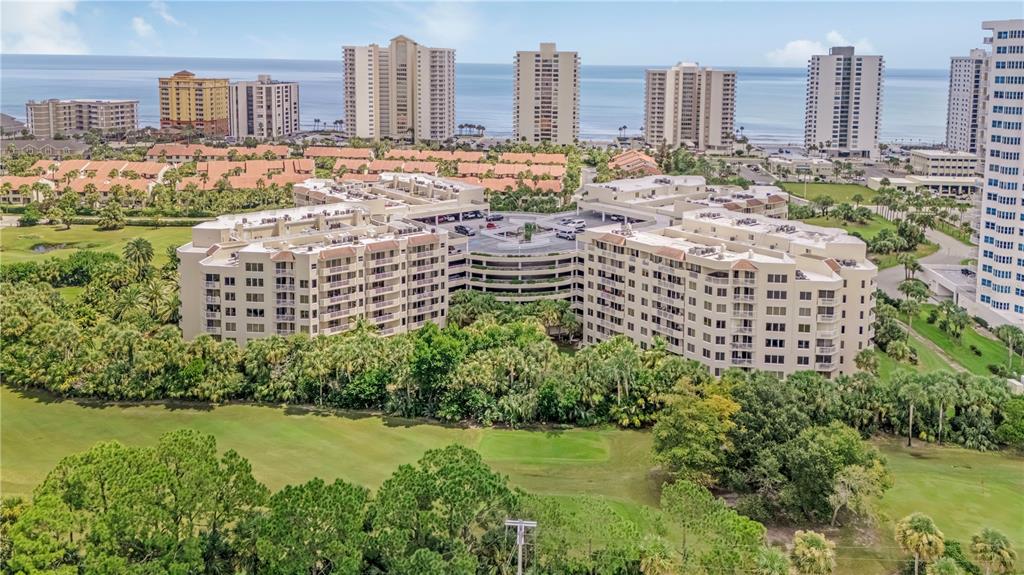 An aerial view of a large multi-story apartment complex surrounded by trees and a golf course — 3 OCEANS WEST BOULEVARD UNIT 2B2, DAYTONA BEACH SHORES, FL