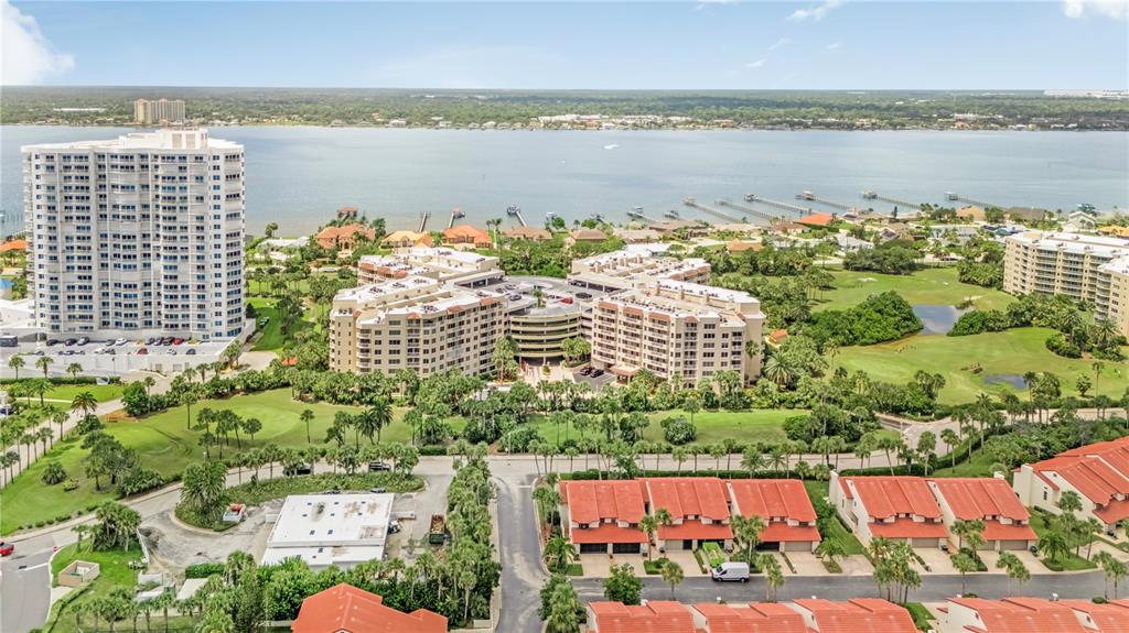 An aerial view shows multi-story apartment buildings, townhomes, and a body of water with docks — 3 OCEANS WEST BOULEVARD UNIT 2B2, DAYTONA BEACH SHORES, FL
