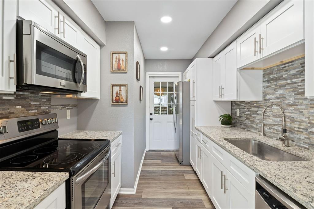 A galley kitchen features white cabinets, granite countertops, stainless steel appliances, and a tiled backsplash — 6305 MORNINGMIST COURT UNIT 6305, TEMPLE TERRACE, FL