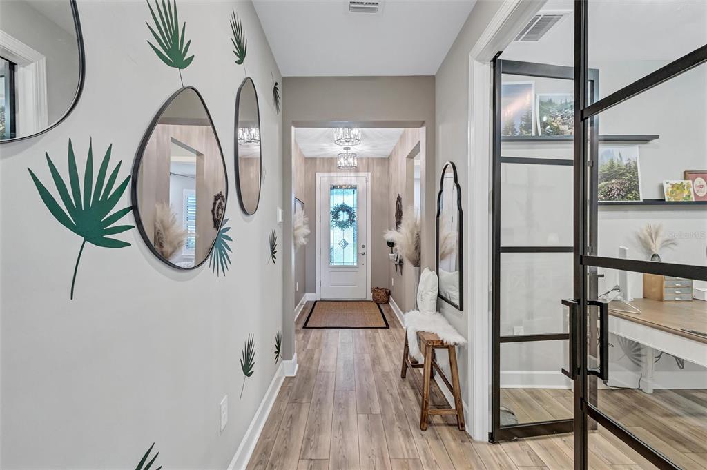 A hallway features wood-look flooring, palm leaf wall decals, several mirrors, and a glass-paned door — 711 PINTAIL COVE, BRADENTON, FL