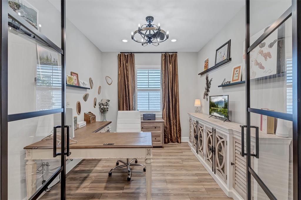 A home office with a wooden desk, white chair, storage cabinet, and glass-paneled double doors — 711 PINTAIL COVE, BRADENTON, FL