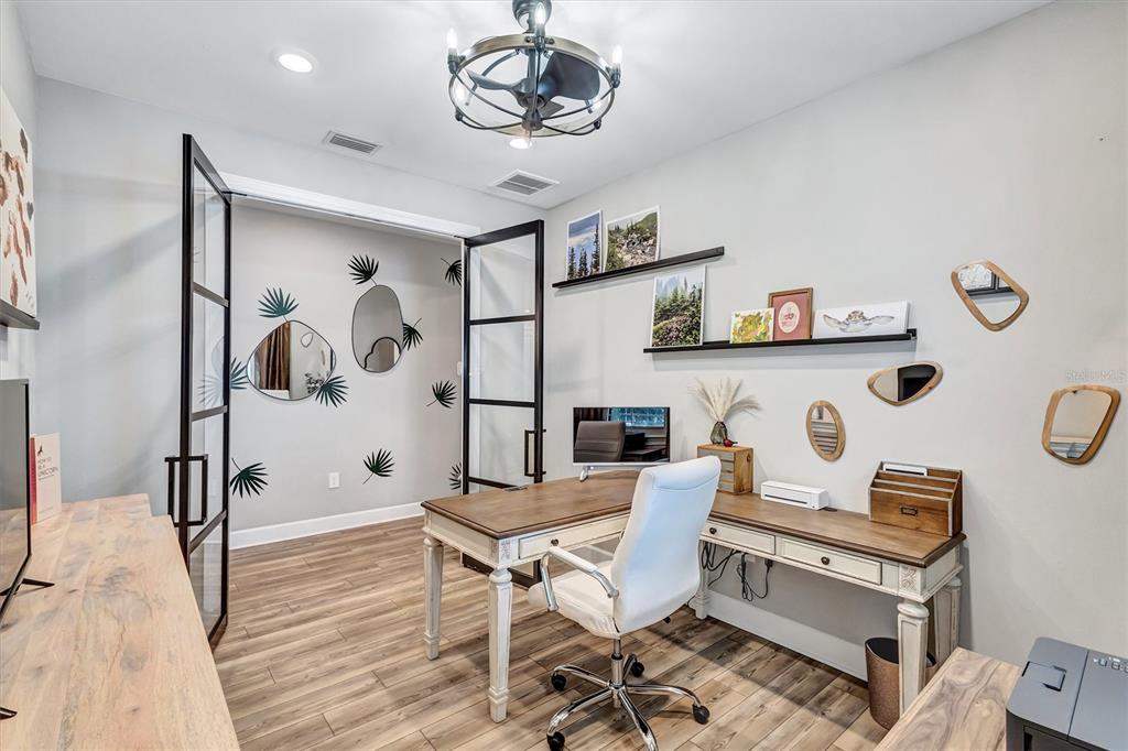 A home office features a wooden desk, a white chair, glass-paned doors, and wall decor — 711 PINTAIL COVE, BRADENTON, FL
