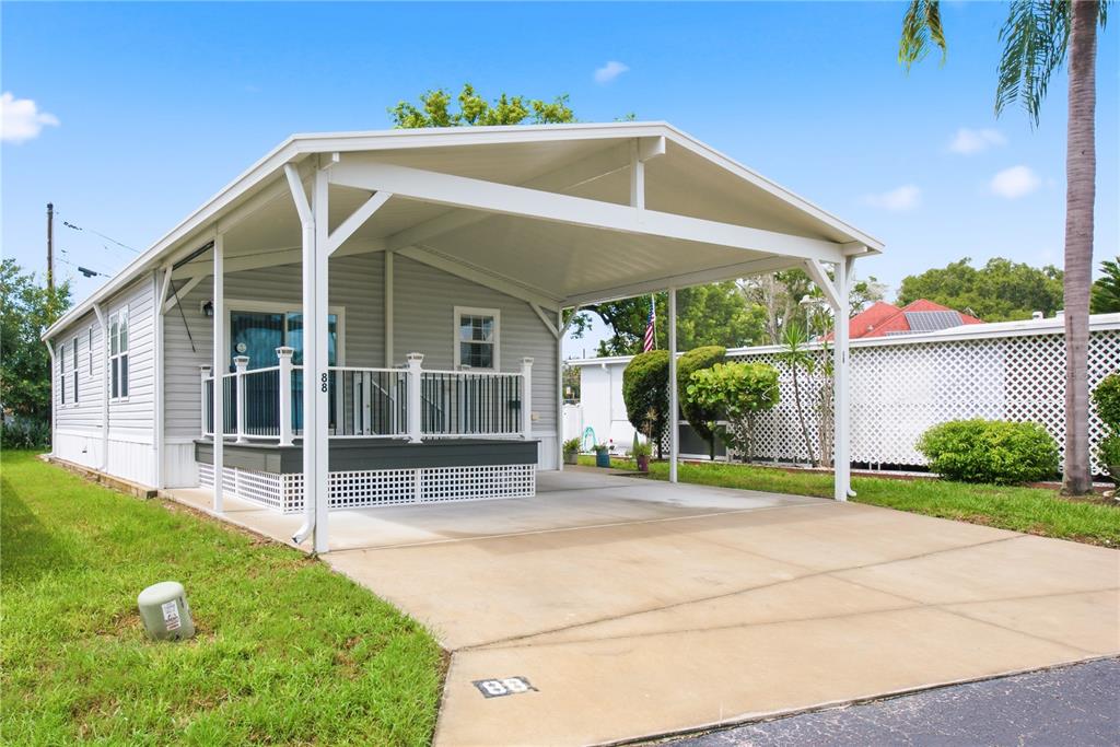 A light gray manufactured home features a covered carport and a small front porch — 980 7TH STREET NW UNIT 88, LARGO, FL