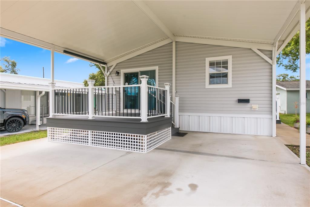 A gray mobile home features a covered carport and a raised deck with black railings — 980 7TH STREET NW UNIT 88, LARGO, FL