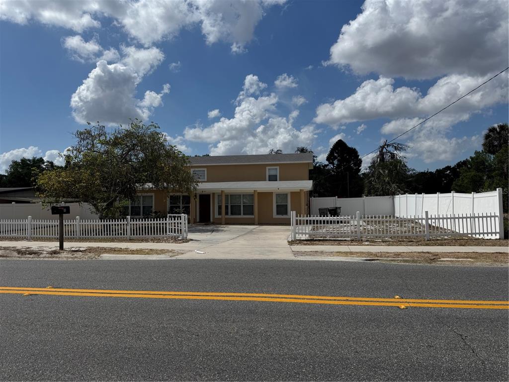 A two-story tan house with a white picket fence sits behind a paved road — 8 E SUMMIT STREET, APOPKA, FL