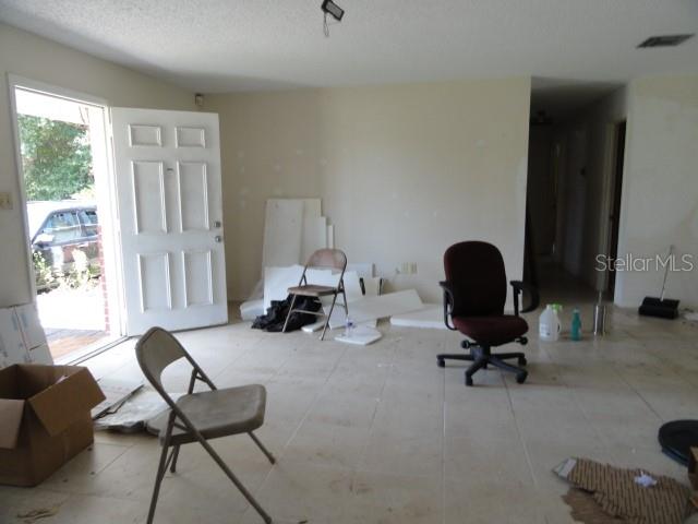 An unfurnished room with tile flooring, a white door, and scattered chairs and debris — 35011 HAINES CREEK ROAD, LEESBURG, FL