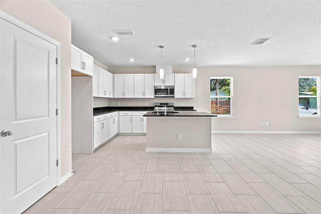A modern kitchen features white cabinets, black countertops, a central island, and light tile flooring — 809 S LOCUST AVENUE, SANFORD, FL