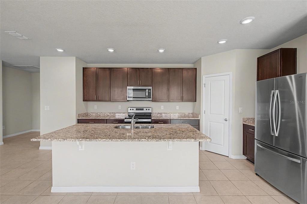 A kitchen features dark wood cabinets, granite countertops, a central island, and stainless steel appliances — 234 LOVELY COURT, PLANT CITY, FL