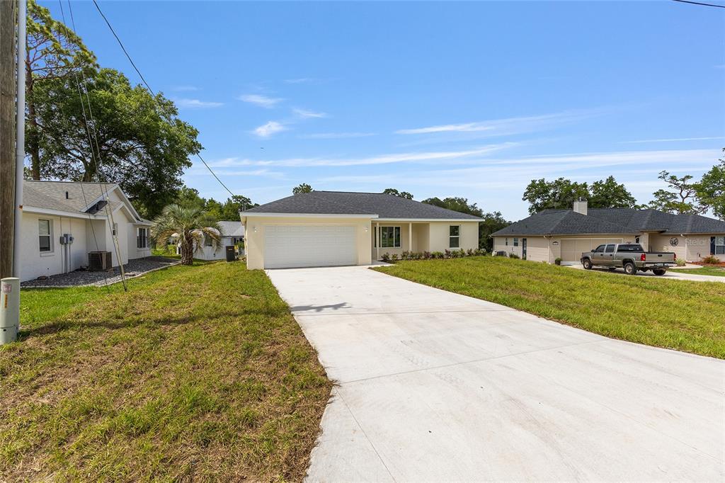 A single-story house with a white garage and concrete driveway under a clear blue sky — 13031 NE 7TH LOOP, SILVER SPRINGS, FL