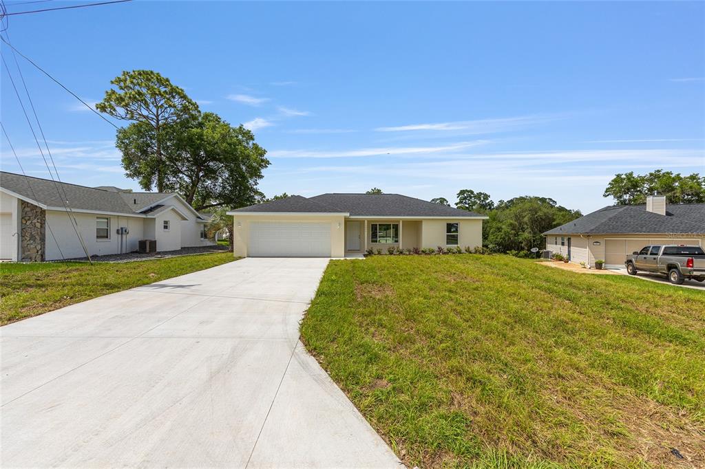 A single-story house with a white garage and a concrete driveway under a blue sky — 13031 NE 7TH LOOP, SILVER SPRINGS, FL