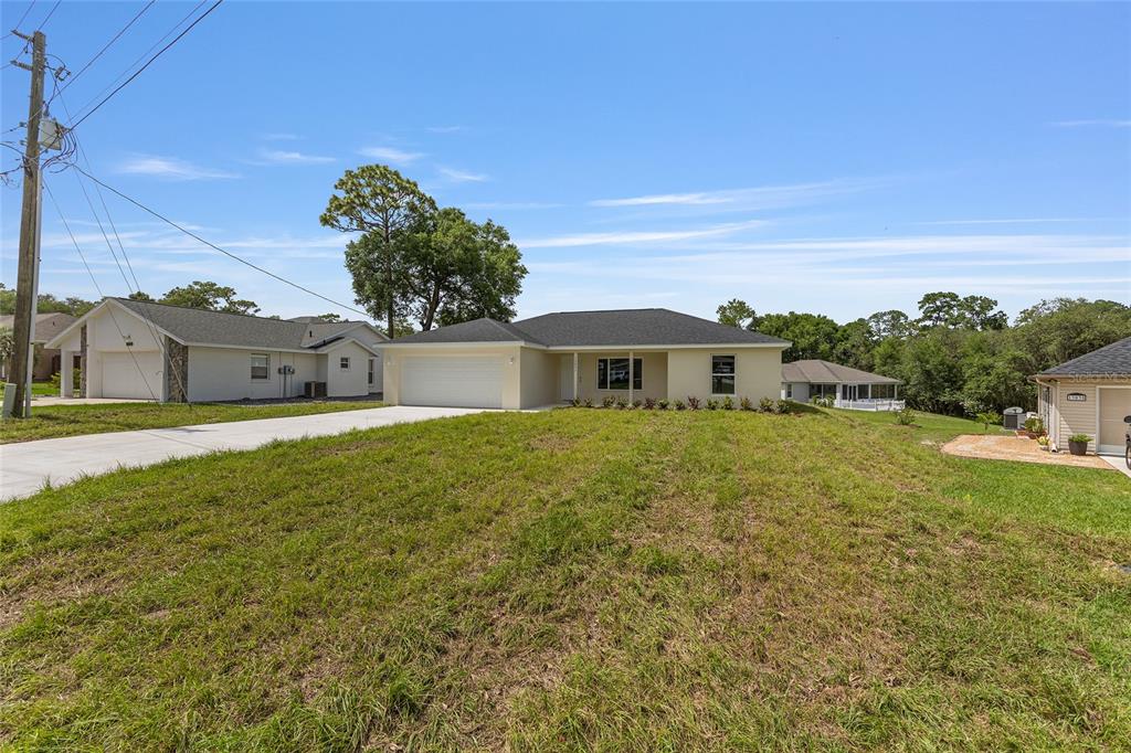 A single-story house with a white garage and light-colored exterior sits on a grassy lot — 13031 NE 7TH LOOP, SILVER SPRINGS, FL