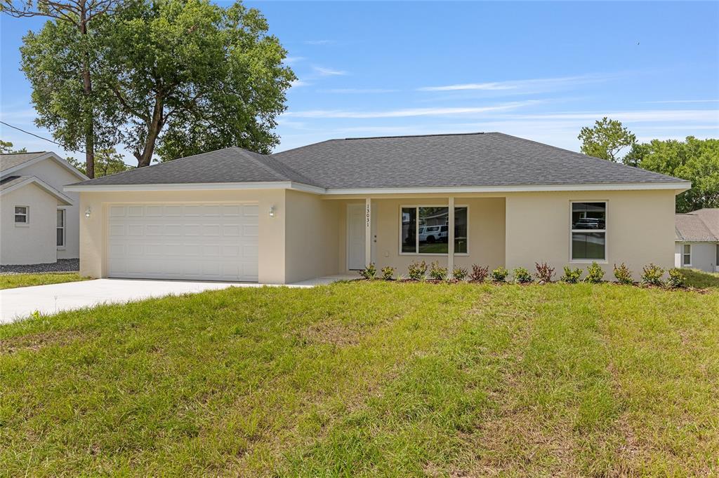 A single-story house with a two-car garage, light-colored stucco exterior, and a dark shingled roof — 13031 NE 7TH LOOP, SILVER SPRINGS, FL