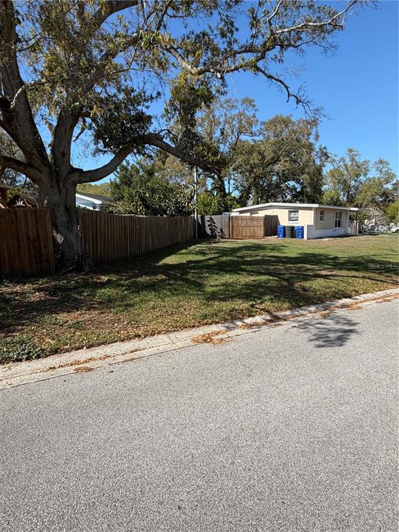 A grassy vacant lot sits next to a wooden fence and a small residential building — 972 CEDARWOOD AVENUE, DUNEDIN, FL