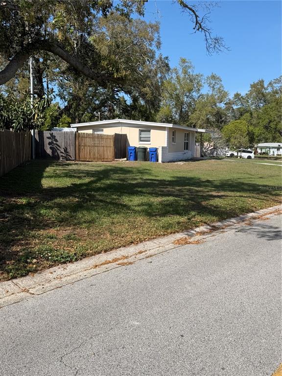 A single-story house with a fenced yard and two blue trash bins sits near a road — 972 CEDARWOOD AVENUE, DUNEDIN, FL