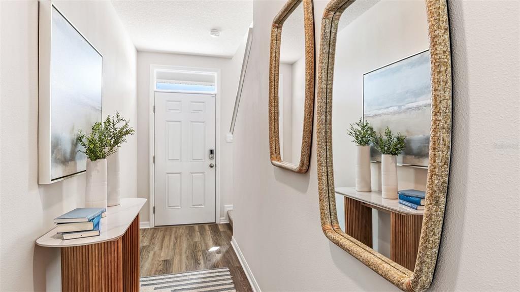 A bright entryway features a white door, wood-look flooring, a console table, and wall mirrors — 7776 42ND LANE N, PINELLAS PARK, FL
