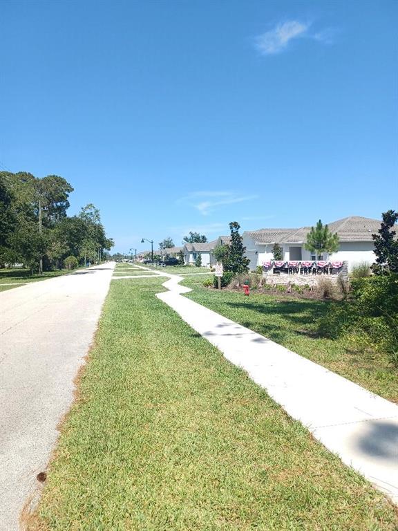 A sidewalk runs alongside a road leading to a residential community entrance sign — 173 RIVER FRONT WAY, EDGEWATER, FL