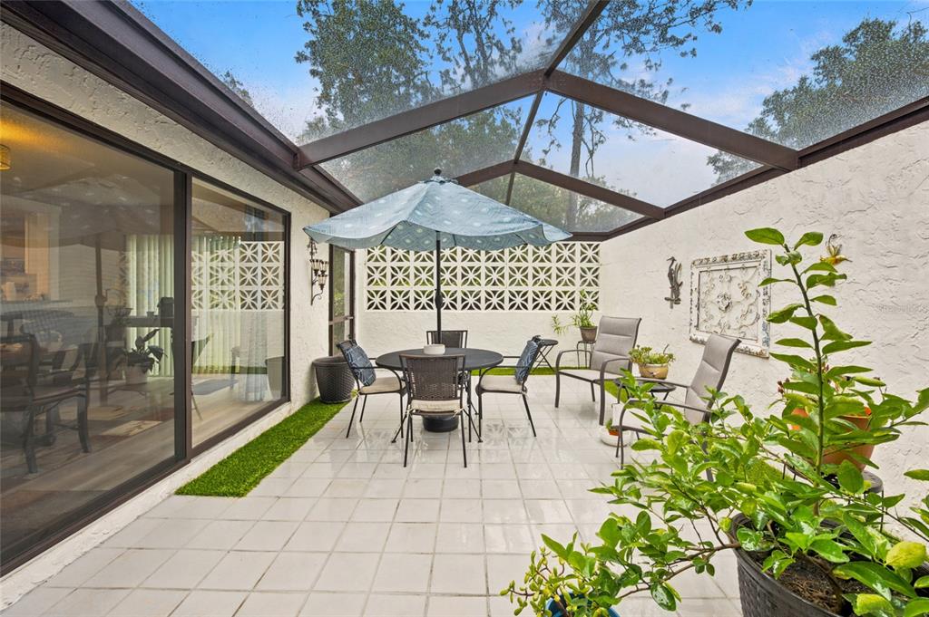A screened-in patio features a tiled floor, a dining set with an umbrella, and decorative walls — 1 QUAIL RUN, HOMOSASSA, FL