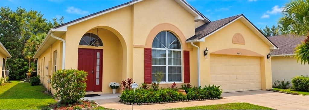 A single-story yellow house with a red front door, arched windows, and a two-car garage — 4640 EAGLE PEAK DRIVE, KISSIMMEE, FL
