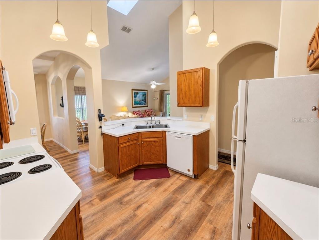 A kitchen with wood cabinets, white countertops, and wood-look flooring, opening into a living area — 4640 EAGLE PEAK DRIVE, KISSIMMEE, FL