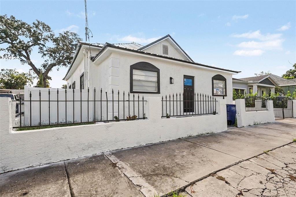 A white stucco house with a black metal fence stands behind a cracked concrete sidewalk — 2923 SANCHEZ STREET, TAMPA, FL