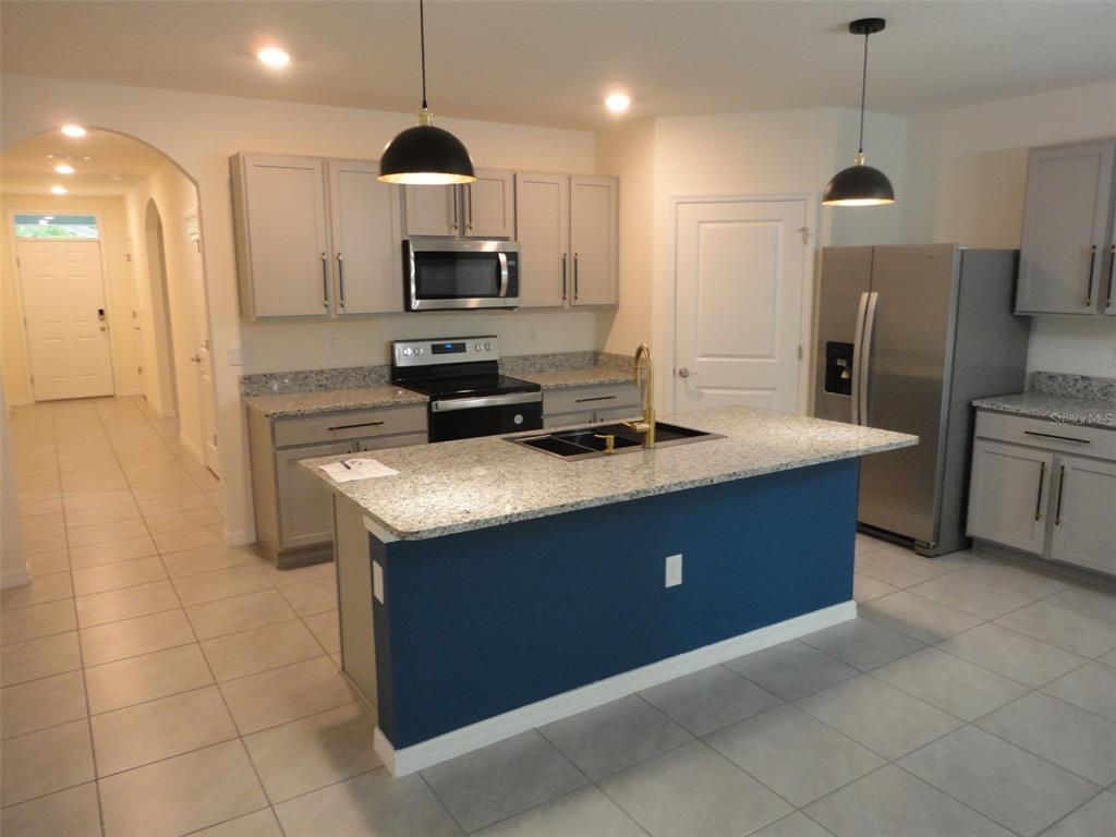 A kitchen features grey cabinets, granite countertops, a blue island, and stainless steel appliances — 216 HICKORY COURSE, OCALA, FL