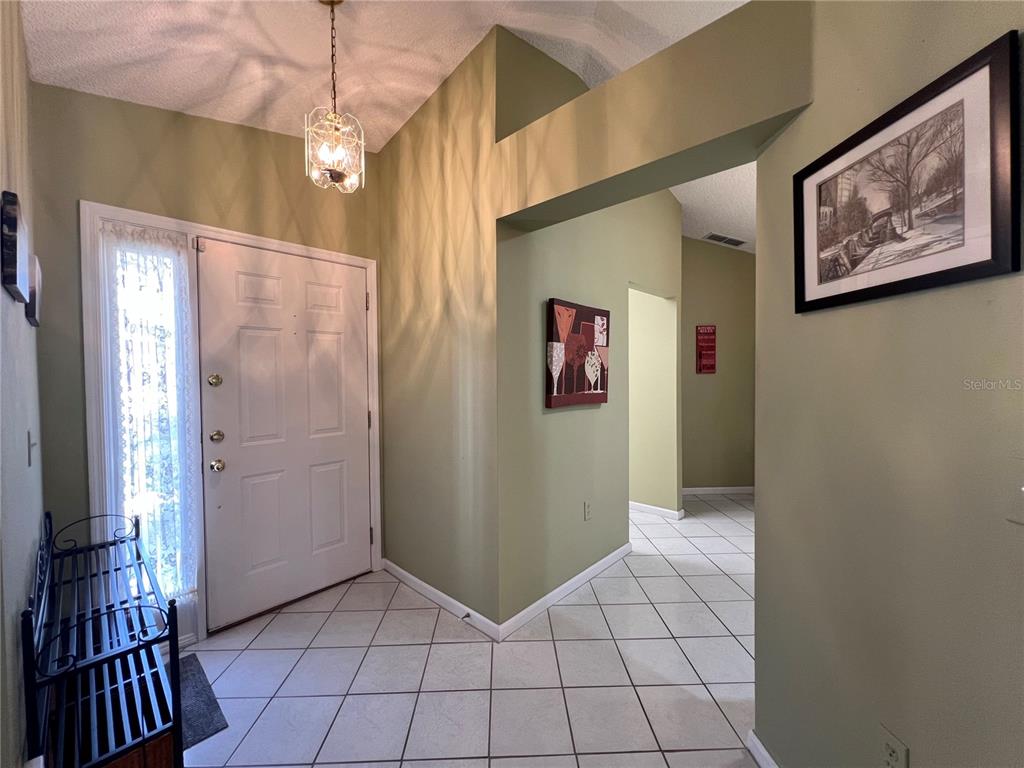 An entryway features light green walls, white tile flooring, a white front door, and a chandelier — 1918 NW 50TH CIRCLE, OCALA, FL