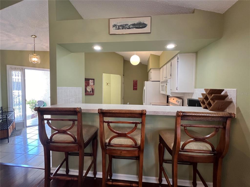 A kitchen features a breakfast bar with three wooden stools and light-colored countertops — 1918 NW 50TH CIRCLE, OCALA, FL