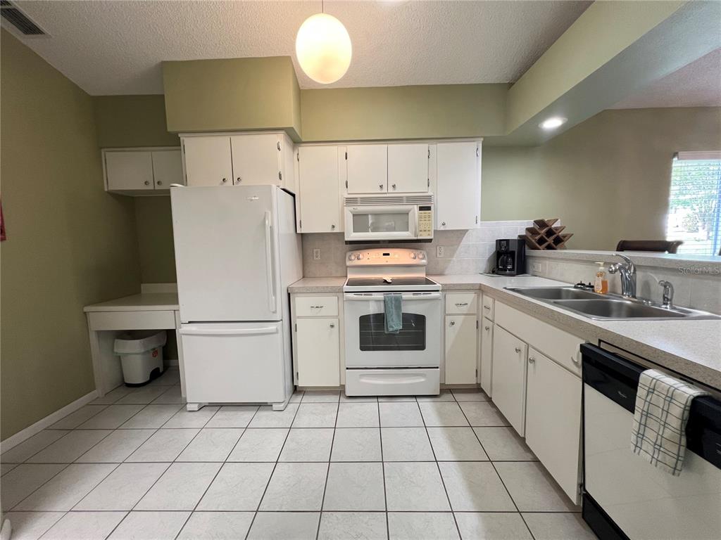 A kitchen features white appliances, white cabinets, tiled flooring, and a double-basin sink — 1918 NW 50TH CIRCLE, OCALA, FL