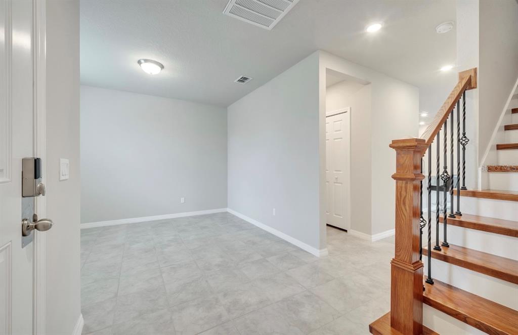 An entryway with light gray tile flooring, a wooden staircase, and a white door — 491 WHISTLING DUCK TRAIL, ST CLOUD, FL