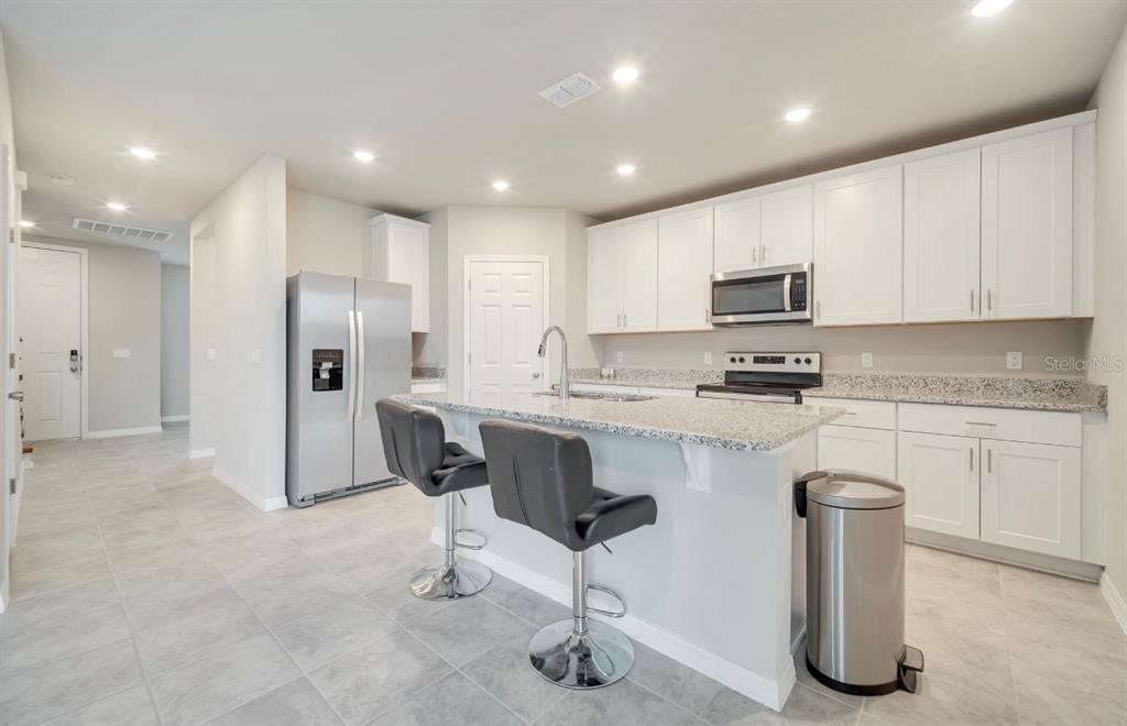A modern kitchen features white cabinets, granite countertops, a center island, and stainless steel appliances — 491 WHISTLING DUCK TRAIL, ST CLOUD, FL